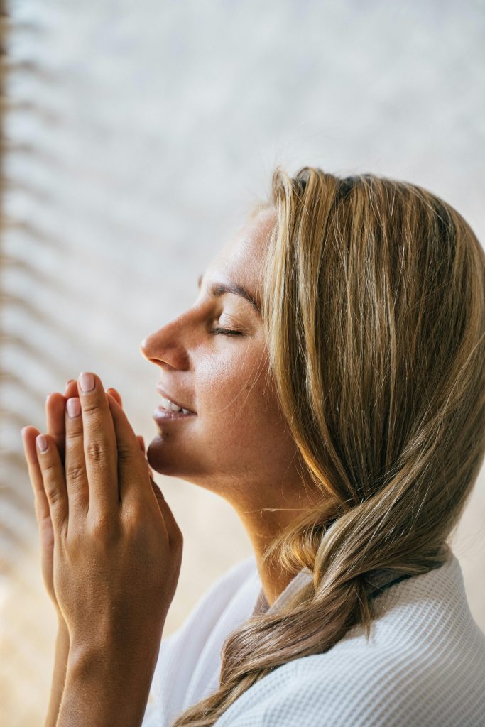 Serene side view portrait of a woman meditating with hands together, basking in natural light.